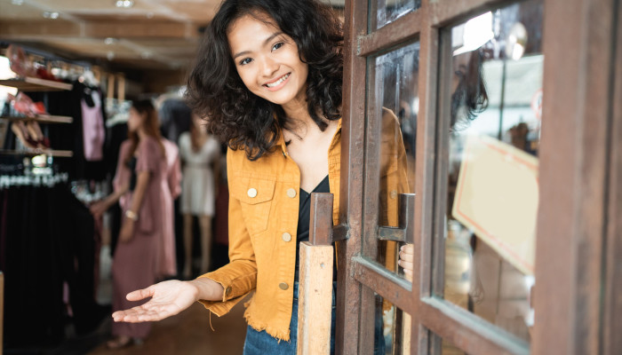A shop worker welcomes customers at the entrance of a British charity shop.