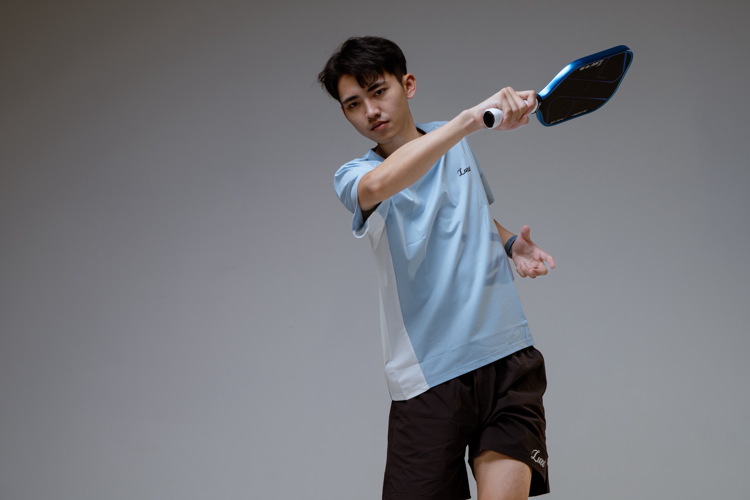 A pickleball player practises a stroke while holding a paddle on an outdoor court.